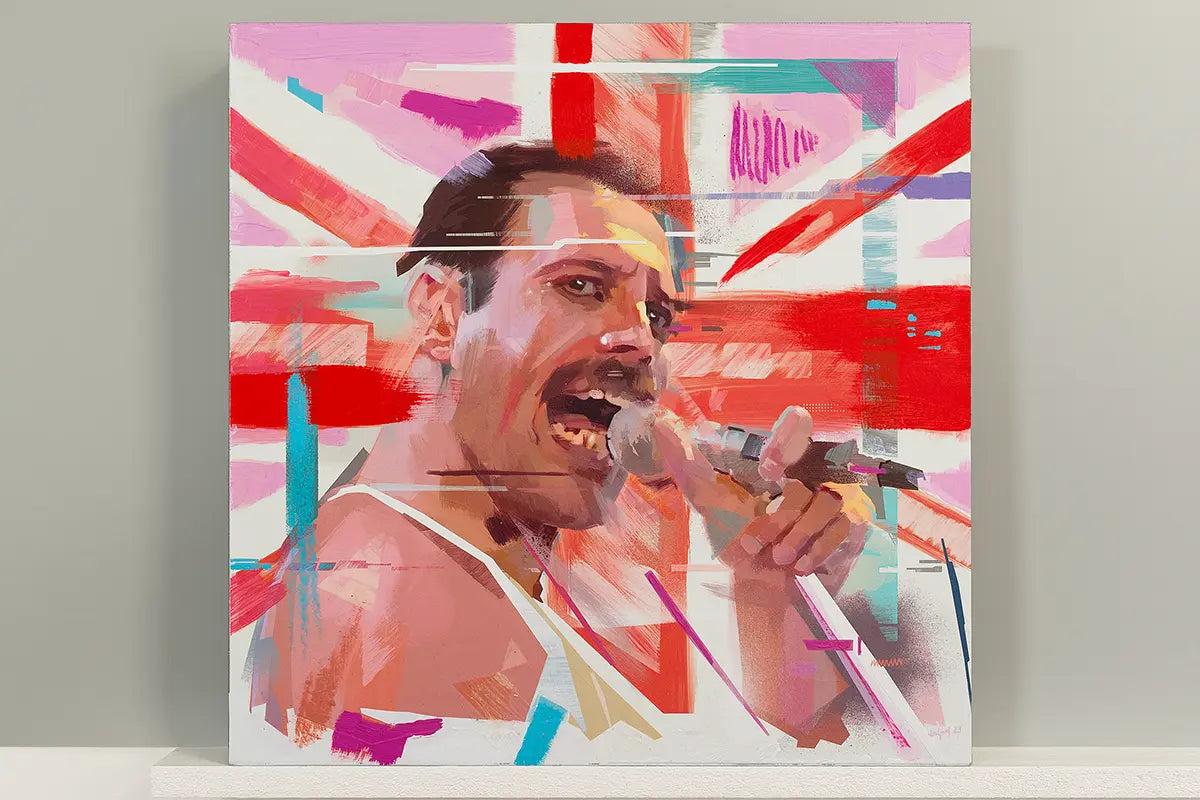 A square canvas art print featuring a stylized, colorful portrait of Freddie Mercury singing into a microphone, set against an abstract background with red, pink, white, and blue brushstrokes. The canvas is displayed leaning against a light gray wall on a white shelf.