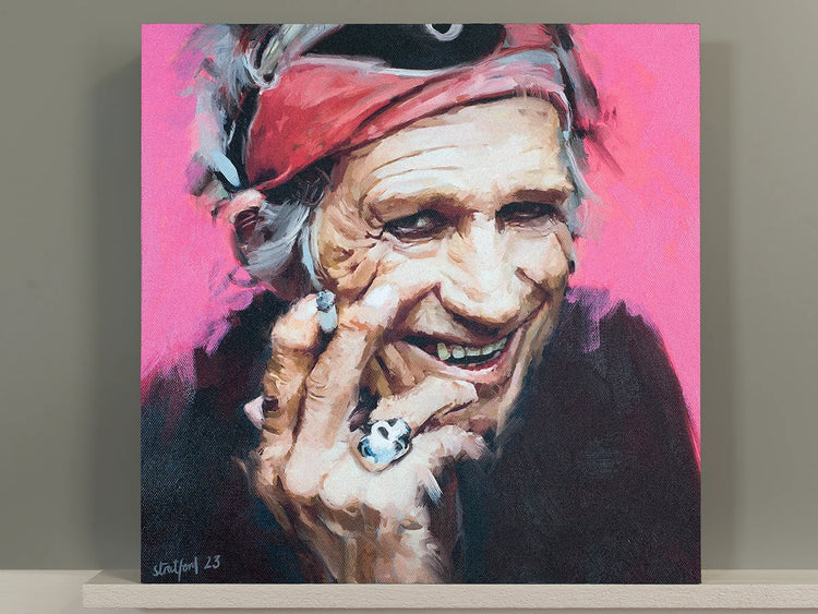 Keith Richards painting with a red bandana against a bright pink background