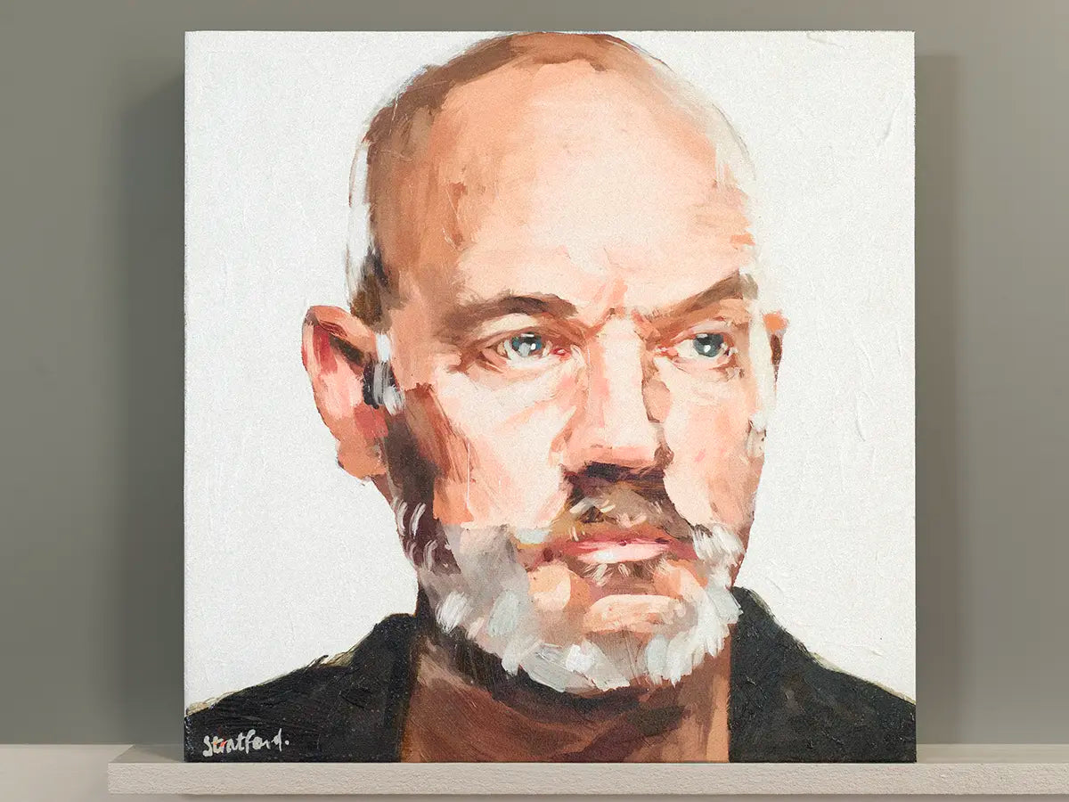A square canvas portrait painting of a Micheal Stipe REM with a white beard, painted in warm beige, brown, and black tones on a white background, displayed against a gray wall on a white shelf.