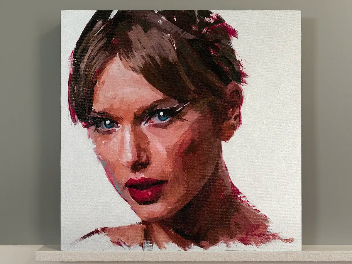 A square canvas painting of a taylor swift, shown leaning against a neutral gray wall on a white shelf. The artwork features expressive brushstrokes in brown, pink, red, and blue tones on a white background.
