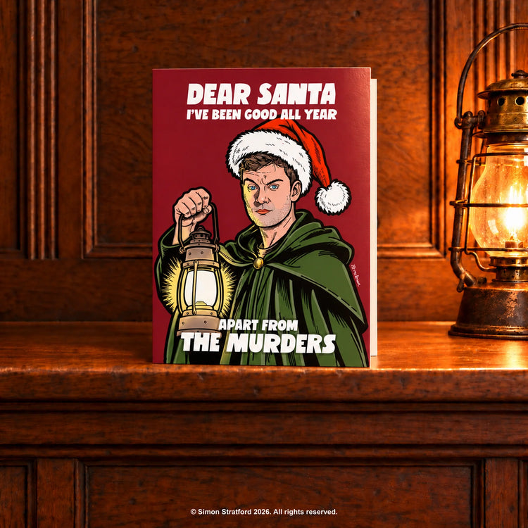 James Acaster Christmas card in a green cloak holding a lantern: Dear Santa, I’ve been good all year. Apart from the murders. Standing slightly open on a wooden mantelpiece beside a glowing antique lamp.
