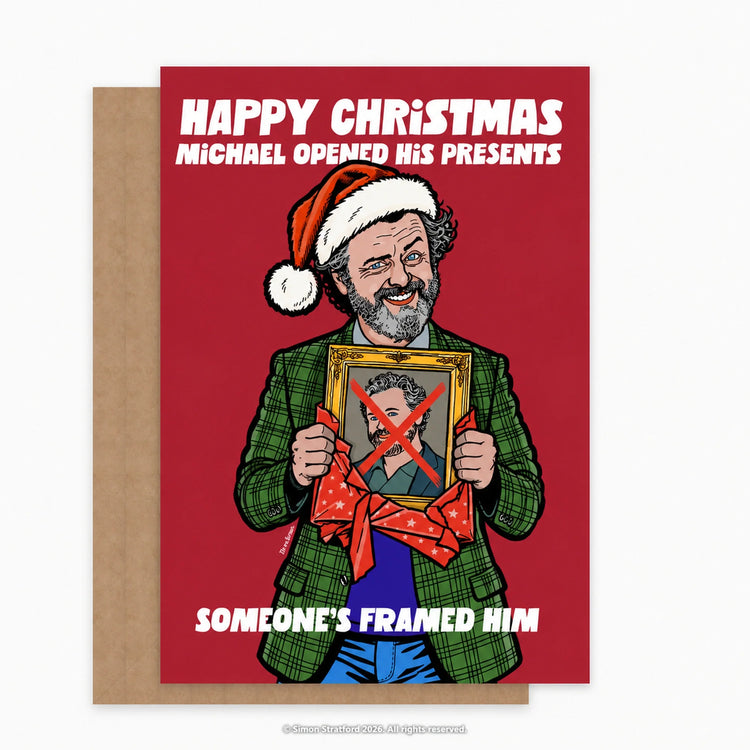 Michael Sheen Christmas card showing him in a Santa hat holding a framed portrait with a red X: Someone’s framed him. Shown with a brown kraft envelope peeking out to the left on a light grey background.