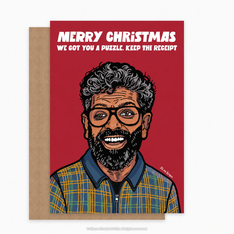 Romesh Ranganathan Christmas card: Merry Christmas. We got you a puzzle. Keep the receipt. Shown with a brown kraft envelope peeking out to the left on a light grey background.